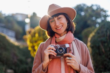 Modaya uygun bir görünüş. Elinde kamera olan genç bir kadın cadde boyunca yürüyor. Kameralı hippi turist kadın. Yaşam tarzı konsepti. film kamerası.