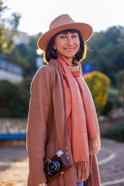 Modaya uygun bir görünüş. Elinde kamera olan genç bir kadın cadde boyunca yürüyor. Kameralı hippi turist kadın. Yaşam tarzı konsepti. film kamerası.