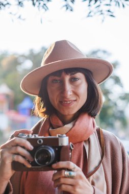 Şık bir görünüş, kameralı genç bir kadın zarif bir şapka ve ceket giyiyor. Hipster bir turist kadın elinde kamerayla fotoğraf çekiyor. film kamerası.