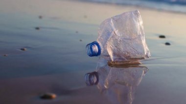 Plastik şişe temiz bir plajın kıyısında. Bir dalga, çöpleri okyanusa atıyor. Plajda bir plastik şişe yatar ve denizi ve deniz yaşamını kirletir..