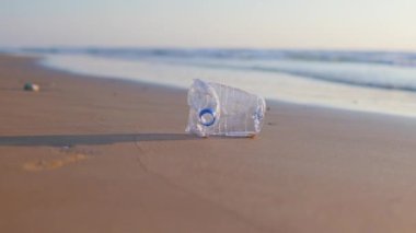 Kız sahildeki çöpleri temizliyor. Plajda plastik şişe. Dalga okyanusa çöp taşır..