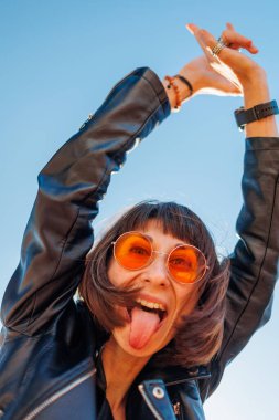 Rock konserinde dans eden bir kız, deri ceketli şık bir kız açık havada dans eden, rock müzik çalan, güneş gözlüklü mutlu bir kadın..