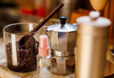 Kahve yapmak için gerekli malzemeler. Moka demliği, fasulye spreyi, kahve değirmeni ve kahve çekirdekleri mutfak masasında duruyor. Kahve yapma konsepti.