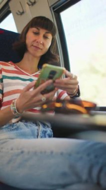 Dikey çekim. Tren yolculuğu. tren yolcusu. Toplu taşıma. Trendeki kadın. Trenle seyahat ederken akıllı telefonlu genç bir kadın. Seyahat kavramının tadını çıkarıyorum. Şık ve şık..