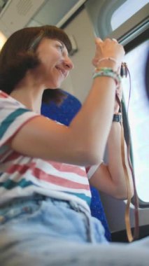 Dikey çekim. Tren yolculuğu. tren yolcusu. Tren yolculuğu. Genç bir kadın, elinde kamerayla tren yolculuğunun tadını çıkarıyor. Turist kamerada güzel turistik yerlerin fotoğraflarını çeker. film kamerası.