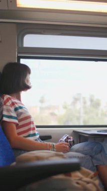 Dikey çekim. Tren yolculuğu. Kameralı genç ve güzel bir kız tren yolculuğunun tadını çıkarıyor ve pencereden dışarı bakıyor. İyi yolculuklar. tren yolcu.