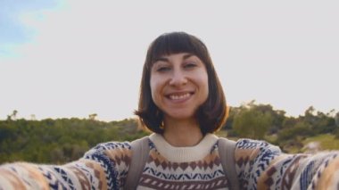 Genç turist, bir dağın tepesinde akıllı telefonuyla fotoğraf çekiyor. Kız dağlarda fotoğraf çekiyor, sonbahar yürüyüşü yapıyor, sırt çantalarıyla. Kız seyahat ediyor. selfie fotoğrafı.