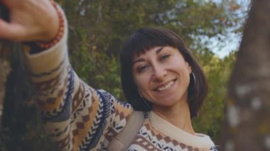 Süslü kazaklı ve sırt çantalı bir kız ormanda yürümekten zevk alıyor. Ormanda yürüyüş yapmak. Sırt çantalı bir kız ormanda yürüyor. Yürüyüş ve yürüyüş. moda ve tarz.