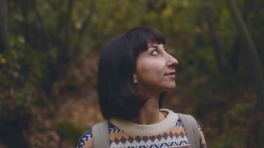 Yürüyüşe çıkmış sırt çantalı bir kadın. Kız etrafına bakar ve gülümser. Dağ yolunda bir gezgin kız. Yaşam tarzı, macera, doğa, aktif yaşam.