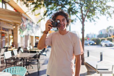 Şehir yürüyüşü sırasında kamerayla gülümseyen genç bir turist. Şehir caddesinde fotoğraf çeken bir fotoğrafçı. Kameralı adam..