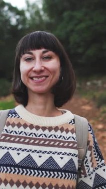 Dikey çekim. Süslü bir kazak giyen ve sırt çantalı bir kız ormanda yürümekten zevk alıyor. Ormanda yürüyüş yapmak. Sırt çantalı bir kız ormanda yürüyor. Yürüyüş ve yürüyüş. moda ve tarz.