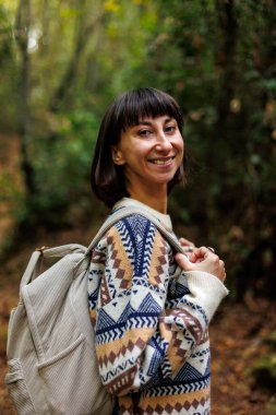 Sırt çantalı kız ormanda yürümekten hoşlanıyor. Ormanda yürüyüş yapmak. Süslü süveter giyen genç bir kız ormanda yürüyor. Yürüyüş ve yürüyüş.