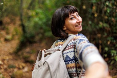 Sırtında sırt çantası ve süveter olan bir kadın seyahat ediyor. Dağlarda bir yürüyüş için. Macera ve yürüyüş. Genç mutlu turist kadın doğada dinleniyor.