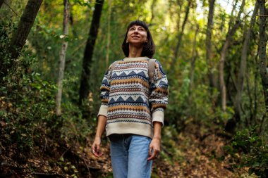Sırtında sırt çantası ve süveter olan bir kadın seyahat ediyor. Dağlarda bir yürüyüş için. Macera ve yürüyüş. Genç mutlu turist kadın doğada dinleniyor.