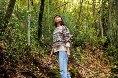 Sırtında sırt çantası ve süveter olan bir kadın seyahat ediyor. Dağlarda bir yürüyüş için. Macera ve yürüyüş. Genç mutlu turist kadın doğada dinleniyor.