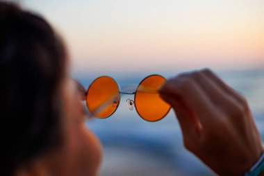 Deniz kenarındaki kız. Kız elinde güneş gözlüğü tutuyor. Genç bir kız deniz kenarında tatilin tadını çıkarıyor..