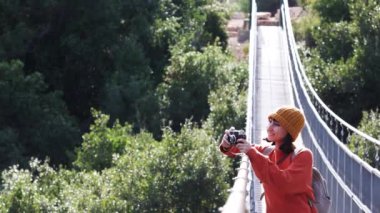 Şapkalı ve sırt çantalı şık genç bir kadın güneşli bir havada kamerayla fotoğraf çekiyor. Seyahat ve fotoğrafçılık. Yolculuğunun tadını çıkaran mutlu bir bayan turist. Sırt çantalı kız..