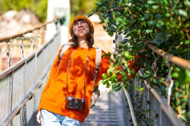 Kameralı ve sırt çantalı genç bir kadın asma köprü boyunca yürümekten hoşlanıyor. Yolculuğunun tadını çıkaran mutlu bir bayan turist. Sırt çantalı kız..