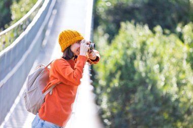 Kameralı ve sırt çantalı genç bir kadın asma köprü boyunca yürümekten hoşlanıyor. Yolculuğunun tadını çıkaran mutlu bir bayan turist. Sırt çantalı kız..
