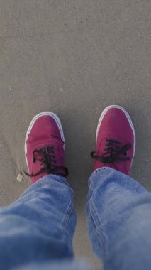 Spor ayakkabılar kumda. Spor ayakkabıların en üst görüntüsü. Kotun ve spor ayakkabının bacağı sahildeki ıslak kumun üzerinde duruyor..