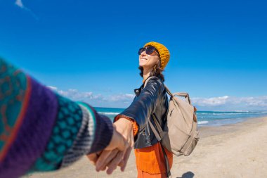 Sahilde erkek arkadaşıyla gezinin tadını çıkaran bir kadın, dikiz manzaralı. Seyahat eden çift. Kız ve erkek el ele tutuşuyor. Sahilde yürü..