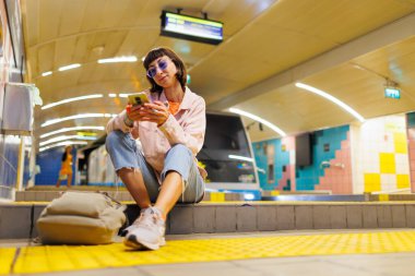 İstasyonda tren bekleyen genç bir kadın. Metrodaki kız. Metroda sırt çantalı şık elbiseli genç bir kız. moda ve tarz.