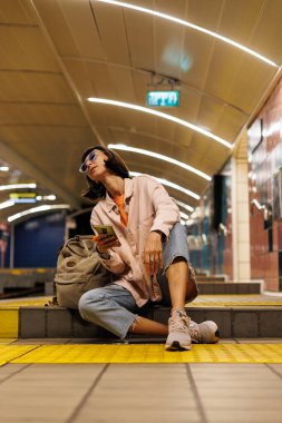 Toplu taşıma araçlarıyla seyahat etmek. İstasyonda tren bekleyen genç bir kadın. Metrodaki kız. Metroda sırt çantalı şık elbiseli genç bir kız. Modern kadın yaşam tarzı.