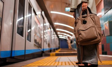Çantası olan kız tren istasyonunda bekliyor. Treni bekle. Metrodaki kız. Şık giyinmiş genç bir kız ve metroda çantası var. Moda çantaları yakın plan. moda ve tarz.