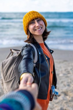 Sahilde erkek arkadaşıyla gezinin tadını çıkaran bir kadın, dikiz manzaralı. Seyahat eden çift. Kız ve erkek el ele tutuşuyor. Sahilde yürü..