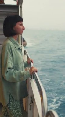 Dikey çekim. Genç bayan bir yolcu gemisinin güvertesinde duruyor ve yolculuğun tadını çıkarıyor. Mutlu kadın. Yatta, tatilde ve seyahatte olan bir kadın. seyahat ve macera.