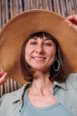 Güzel, gezgin, esmer bir kadının yakın plan portresi. Şapkalı, şık yaz kıyafetleri giyiyor. Yaz tatili boyunca sahilde gülümseyen neşeli genç bir kadın. Mutlu kız.