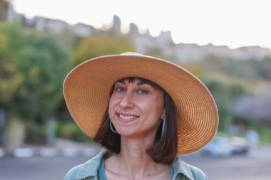 Genç bir esmer şehirde dururken mutlu bir şekilde gülümsüyor. Gömlekli, etekli ve şapkalı şık bir kız avlunun yanında duruyor. Yaz Portresi