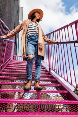 Şehirde şapkalı şık bir kız merdivenlerden aşağı iniyor. Moda tarzı.