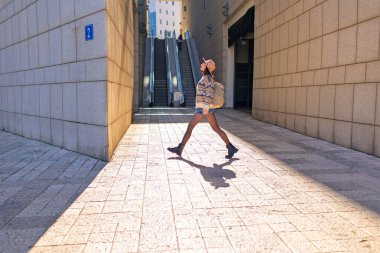 Şehirde sırt çantalı bir kız. Binaların arasında cadde boyunca yürüyen mutlu genç bir kadın. Sırt çantalı bir bayan gezgin şehri geziyor, şık bir kız şehirde dolaşıyor..