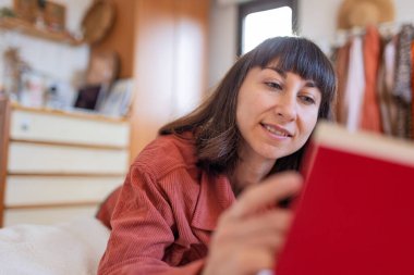 Mutlu kız kanepede oturup kitap okuyor, evde gülümsüyor, rahatlıyor, boş zaman, ev hayatı ve yaşam tarzı. Odadaki kanepede kitap okuyan pozitif bir kadın..