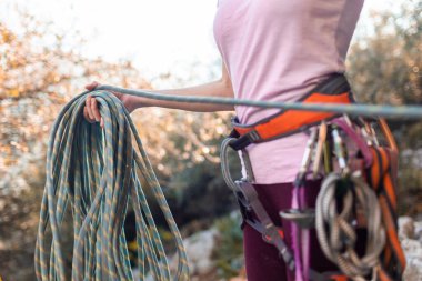 climber winding rope after climbing. Close-up of a rock climber in harness and climbing equipment outdoors. Alpinism and rock climbing clipart