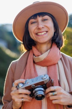 Şık bir görünüş, kameralı genç bir kadın zarif bir şapka ve ceket giyiyor. Hipster bir turist kadın elinde kamerayla fotoğraf çekiyor. film kamerası.