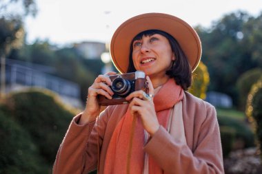 Modaya uygun bir görünüş. Elinde kamera olan genç bir kadın cadde boyunca yürüyor. Kameralı hippi turist kadın. Yaşam tarzı konsepti. film kamerası.