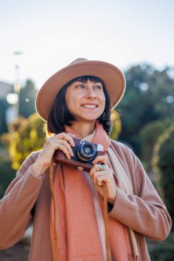 Modaya uygun bir görünüş. Elinde kamera olan genç bir kadın cadde boyunca yürüyor. Kameralı hippi turist kadın. Yaşam tarzı konsepti. film kamerası.