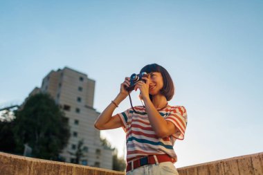 Kameralı genç bir kız. Moda ve çekici, analog film kamerası olan güzel bir kadın gün batımında fotoğraf çekiyor.,