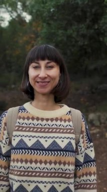 Sırt çantalı, doğa yürüyüşü yapan gülümseyen bir kadın. Şık bir kazak giyen genç bir turist bir dağ yolunda duruyor ve kameraya bakıp gülümsüyor. Yaşam tarzı, macera, doğa, aktif yaşam. 