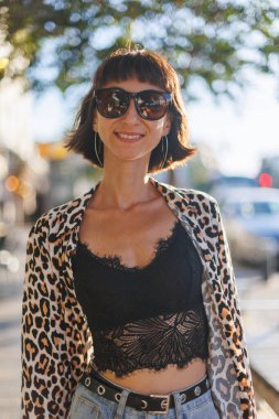 Leopar desenli bluz giyen neşeli genç bir kadın bir yaz günü sokakta yürür. Şehirde yürü..