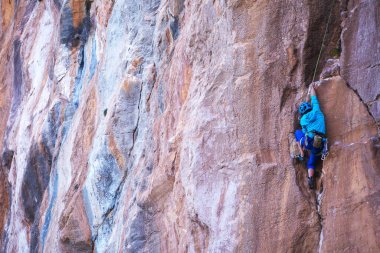 Kasklı bir kadın güzel mavi bir kayaya tırmanır. Koruyucu ekipmana tırmanıyorum. Tırmanırken güvenlik. Kaya tırmanışçısı doğal bir arazide zorlu bir rotanın üstesinden gelir. Türkiye 'de kaya tırmanışı.