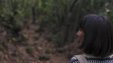 Kız gülümser ve kameraya bakar. Sırt çantalı kız ormanda yürümekten hoşlanıyor. Ormanda yürüyüş. Sırt çantalı genç bir kız ormanda yürüyor. Yürüyüş ve yürüyüş. 