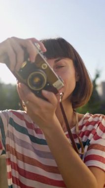 Dikey çekim. Genç bir kız kamera kullanıyor. Fotoğrafçı kamerayı ayarlar. Film kamerası olan şık bir kız. Film kamerası kapat. Maceralar ve seyahat.