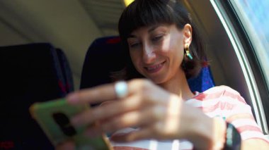 Trendeki kadın telefon kullanıyor. Trenle seyahat ederken akıllı telefonlu genç bir kadın. Toplu taşıma. seyahat konsepti. Şık ve şık..