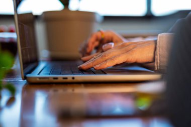 Laptop kullanan bir kızın elinin yan görüntüsü. Bitkileri olan şık bir ofis. Genç bir kadının ellerine yakın çekim. Uzaktan çalışıyor. İş konsepti ve pazarlama.