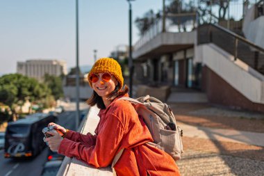 Kameralı mutlu kız şehirde dolaşıyor. Genç turist şehri geziyor ve geziyor. Şehirde dolaşan bir turist..
