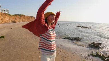 Gülümseyen neşeli kız sahilde eğleniyor anın tadını çıkarıyor. Plajda yürüyen tişörtlü bir kadın. Tatilde bir turist. Seyahat ve macera.