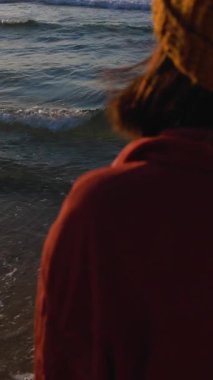 Dikey çekim. Gün batımında okyanusa bakıp hayatı düşünen bir kadın. Arkadan bak. Havalı kız okyanusa bakıyor, kız tatilin ve seyahatin tadını çıkarıyor..